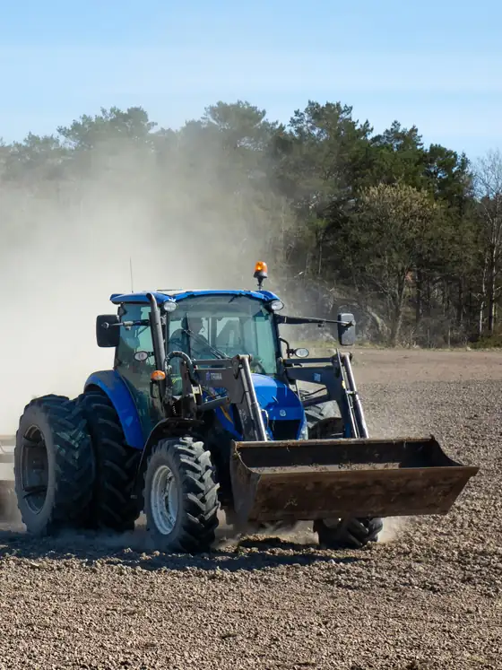 A blue tractor pulling a roller across a dry field, raising dust