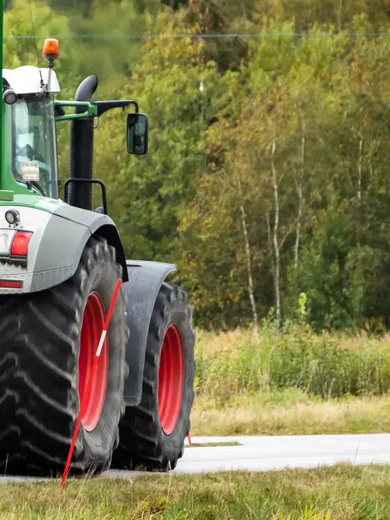 The rear wheels and cab of a large tractor towing a trailer along a country road